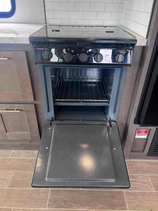 RV rental kitchen features a compact Suburban stove and oven with the door open, showcasing the racks inside.. Forest River Georgetown 2022