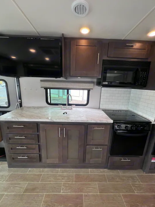 Check out this RV rental's modern kitchen! It has dark cabinets, a white counter with a sink, microwave, stove, and TV.. Forest River Georgetown 2022