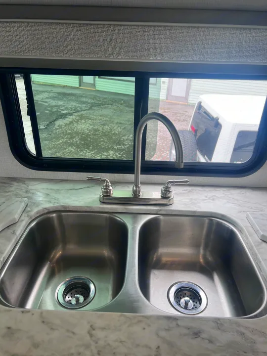 Clean RV rental kitchen with a double sink, gooseneck faucet, and countertop. Window shows outside view.. Forest River Georgetown 2022