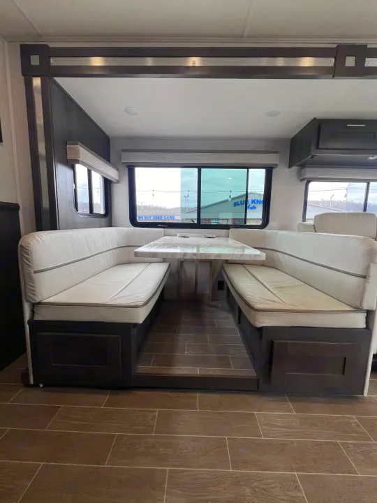 Inside a modern rv rental: U-shaped dinette with white cushions, marble-look table, and dark wood flooring.. Forest River Georgetown 2022
