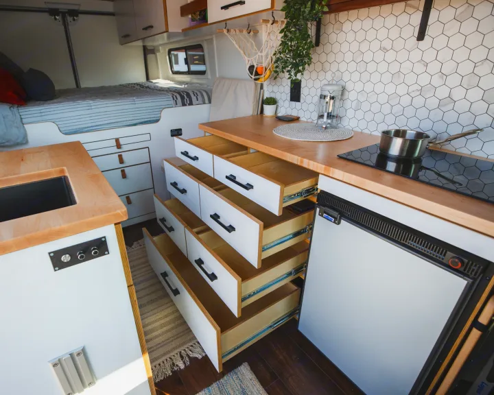 Cozy RV rental interior featuring a modern kitchen with induction stove, sink, refrigerator, and organized pull-out storage drawers.. Dodge Ram Promaster 2021