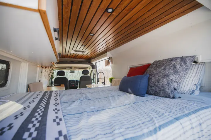 Step inside this cozy RV rental camper van, featuring a comfy bed, stylish wood ceiling, and functional front cabin area.. Dodge Ram Promaster 2021