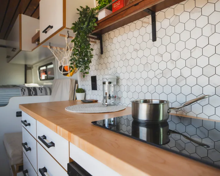 Modern RV rental kitchen with wood counters, induction stove, white hex tile backsplash, and hanging fruit basket.. Dodge Ram Promaster 2021