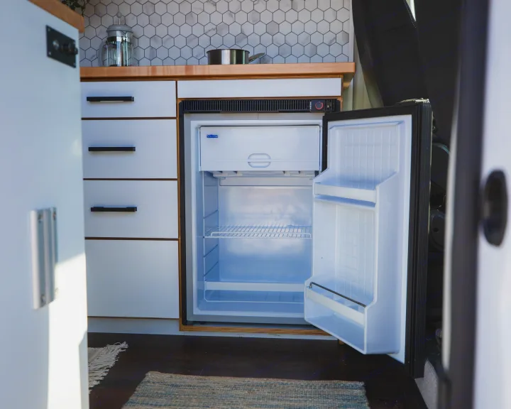 RV rental kitchen showcasing a compact, open refrigerator, white cabinets, wood counter, and tile backsplash.. Dodge Ram Promaster 2021