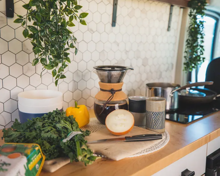 RV rental kitchen counter with fresh kale, bell pepper, onion, coffee maker, and cooking pots for healthy meals.. Dodge Ram Promaster 2021