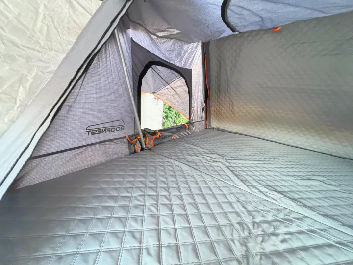 Inside a Roofnest roof-top tent: comfortable quilted mattress, storage, and an outside view. Ideal for your RV rental trip.. Ady ORT 2022