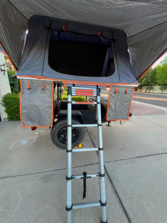 Grey and orange rooftop tent on a trailer, with its extended ladder. Perfect for an RV rental outdoor adventure.. Ady ORT 2022