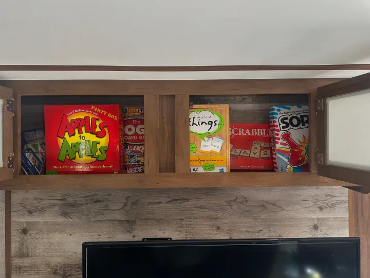 RV rental storage: cabinet filled with popular board games like Apples to Apples, Scrabble, and Sorry!, perfect for travel fun.. Gulf Stream Envision 2020