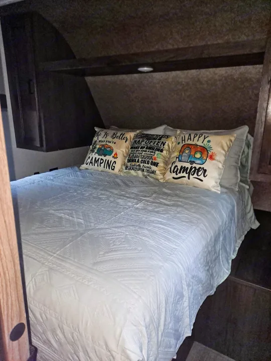 Cozy RV rental bedroom with a comfy bed, white quilt, and fun camping-themed pillows. Perfect for your next adventure!. Highland Ridge RV Open Range 2021