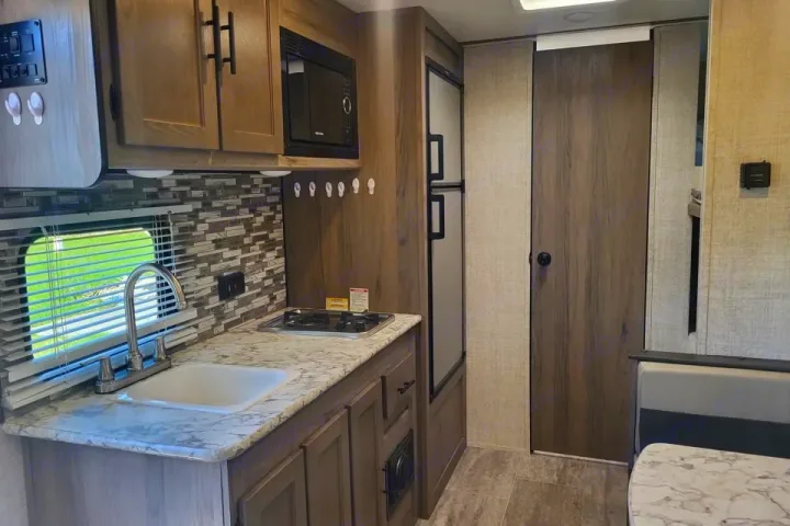 Modern RV rental interior features a functional kitchen with sink, stove, microwave, fridge, and a dining nook.. Grand River Bunkhouse Ultra-Lite Series 2020