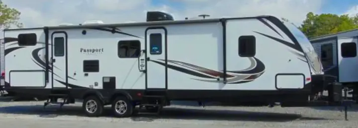 White Passport travel trailer, a spacious RV rental. Features black/brown graphics, multiple windows, and two entry doors.. Keystone RV Passport Grand Touring 2018