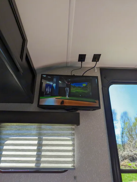 RV rental interior: wall-mounted TV with golf simulator gameplay. Blinds cover the window for comfort in this mobile retreat.. Forest River Cherokee Wolf Pup 2022