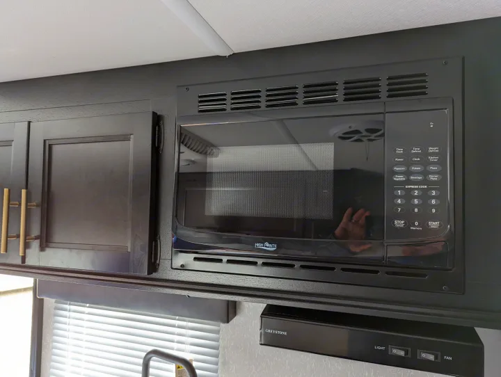 RV rental kitchen features a black High Pointe microwave above a Greystone range hood, surrounded by dark cabinets.. Forest River Cherokee Wolf Pup 2022