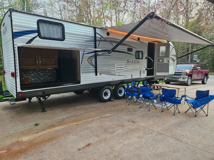 Spacious travel trailer RV rental parked with an open outdoor kitchen, extended lighted awning, and blue camp chairs set up.. Forest River Salem 2017