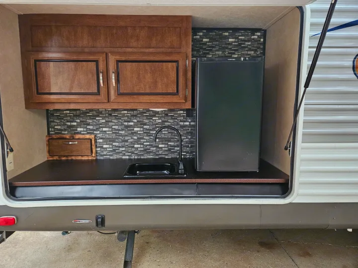 Explore this RV rental's outdoor kitchen: a mini-fridge, sink, and wood cabinets, perfect for adventures.. Forest River Salem 2017