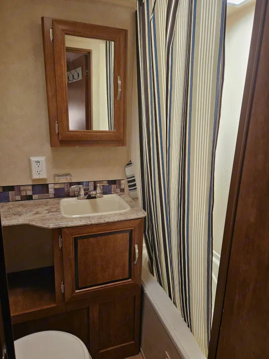 Compact RV rental bathroom featuring a vanity, sink, mirror, and striped shower curtain for functional use.. Forest River Salem 2017