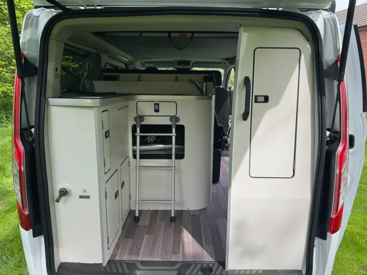 Explore this RV rental's well-designed campervan interior, featuring a modular kitchenette, storage, and ladder to a bunk bed.. Ford Nugget 2022