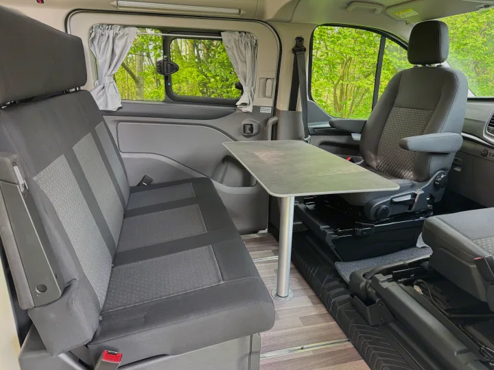 RV rental interior: A compact living space with a table, bench seating, and swivel passenger seat for travel.. Ford Nugget 2022