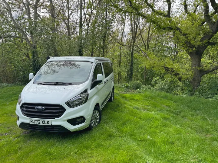 White Ford Transit Custom Westfalia camper van on grass by trees.. Ford Nugget 2022