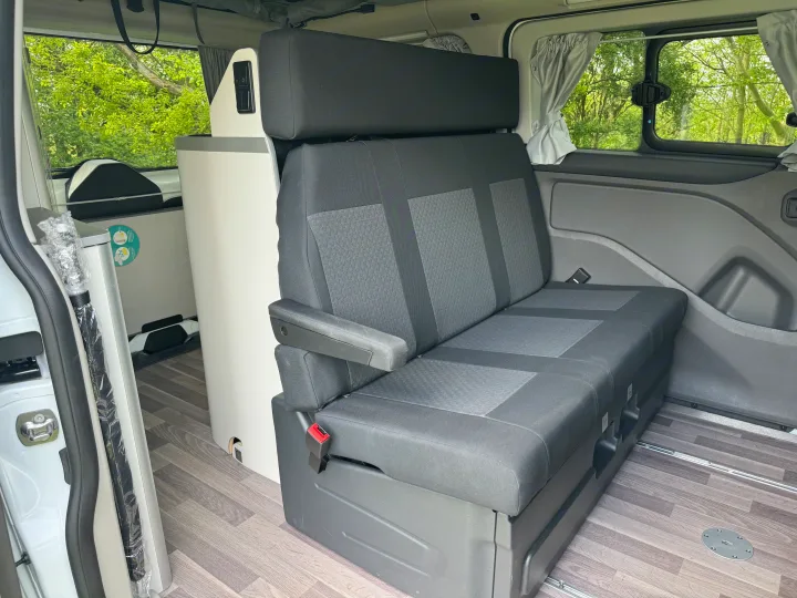 RV rental: Inside a modern camper van with convertible bench seats, integrated storage, and windows showing green trees.. Ford Nugget 2022
