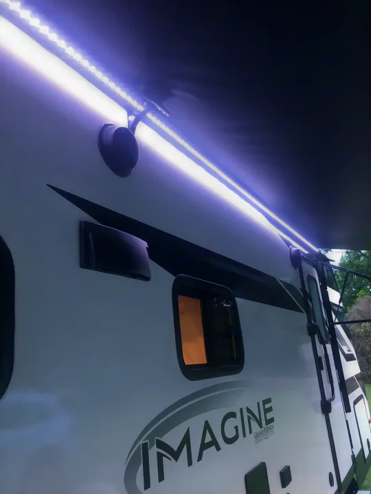 Night view of a Grand Design Imagine RV rental with bright LED awning lights, perfect for camping.. Grand Design Imagine 2023