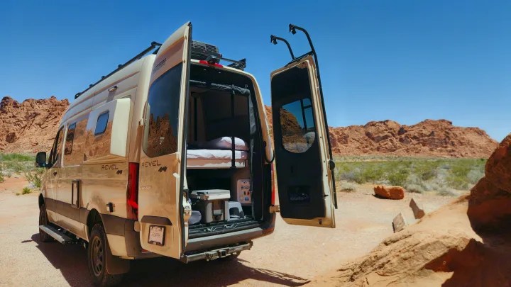 An RV rental Winnebago Revel 4x4 camper van with open back doors reveals bunk beds, parked in a vibrant red rock desert. Adventure awaits!. Winnebago Revel 2024