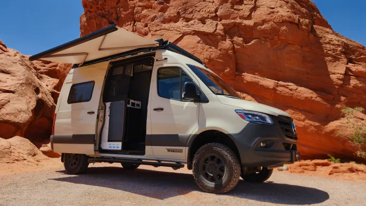 White Winnebago camper van, ideal for rv rental, parked by red rocks. Side door open to interior, awning extended for shade.. Winnebago Revel 2024
