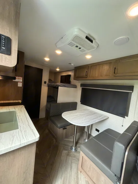 Inside a modern RV rental featuring a kitchen with a marble-patterned counter, dinette, comfy bunk beds, and ceiling AC unit.. Olympia Sport 19BH 2022