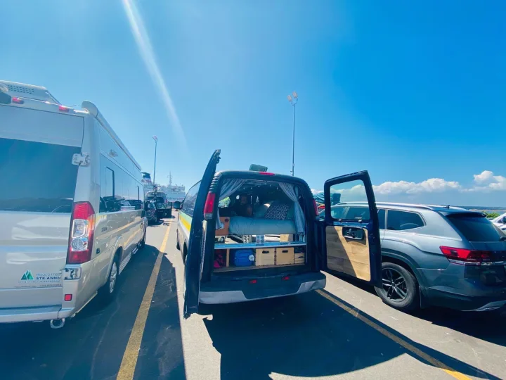 RV rental and a custom camper van with open doors, showing a bed, parked on a sunny day at a ferry terminal.. Chevrolet Express 2001