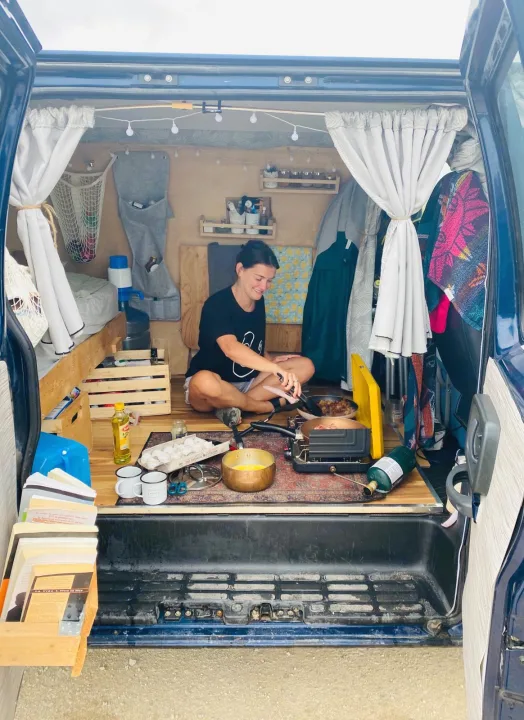 RV rental: Woman cooking on a portable stove in her cozy, organized camper van interior.. Chevrolet Express 2001