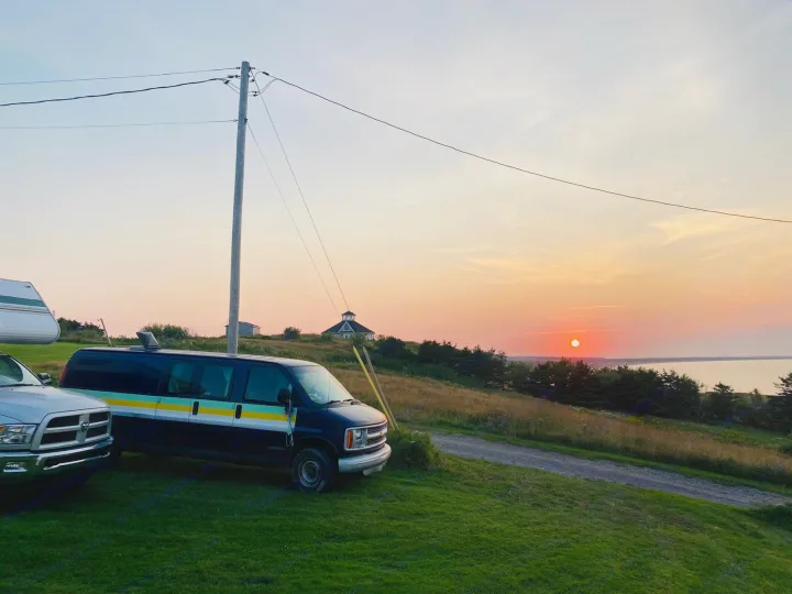 Serene sunset over water, ideal for RV rental adventures. Camper van & RV trailer parked amidst grassy hills.. Chevrolet Express 2001