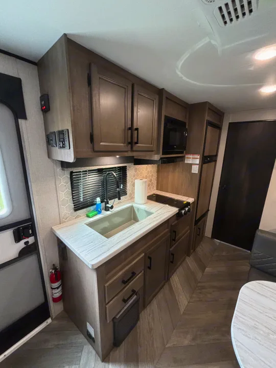 Inside an RV rental, featuring a functional kitchen with sink, stovetop, microwave, cabinets, and control panels.. Olympia Sport 19BH 2022