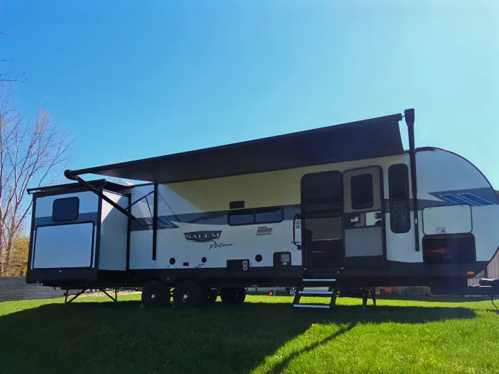 White Salem Platinum RV rental trailer with extended awning, open door, and slide-out on grass under a blue sky.. Forest River Salem Platinum 2023