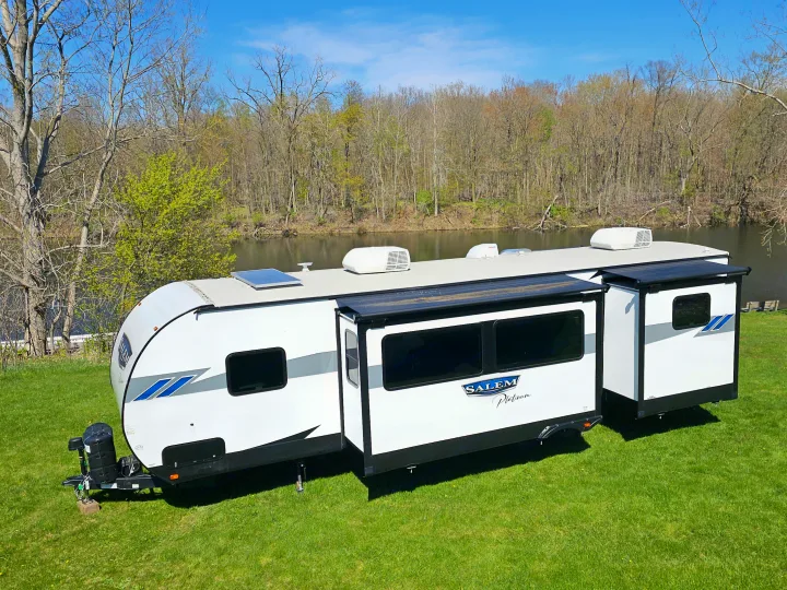 White travel trailer RV rental with slide-outs, parked by a river, perfect for scenic camping.. Forest River Salem Platinum 2023