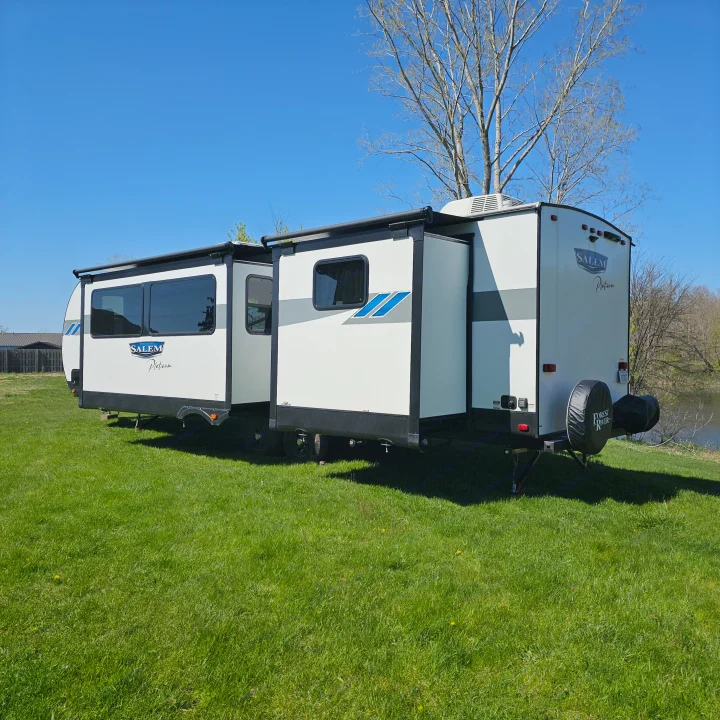Salem Platinum RV rental parked on green grass by a lake, slide-outs extended under a clear blue sky.. Forest River Salem Platinum 2023