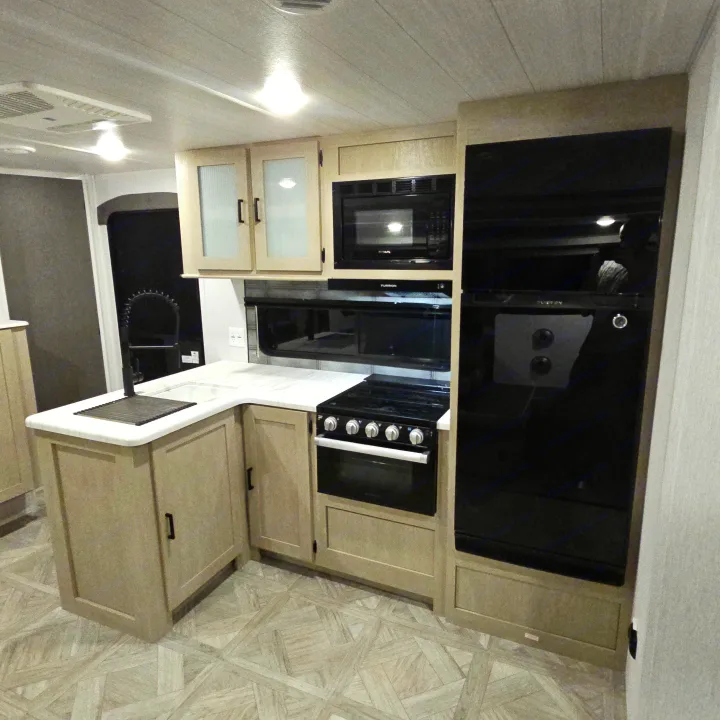 Compact RV rental kitchen with light cabinets, white counters, stove, microwave, and large fridge for easy meal prep on the road.. Forest River Salem Platinum 2023