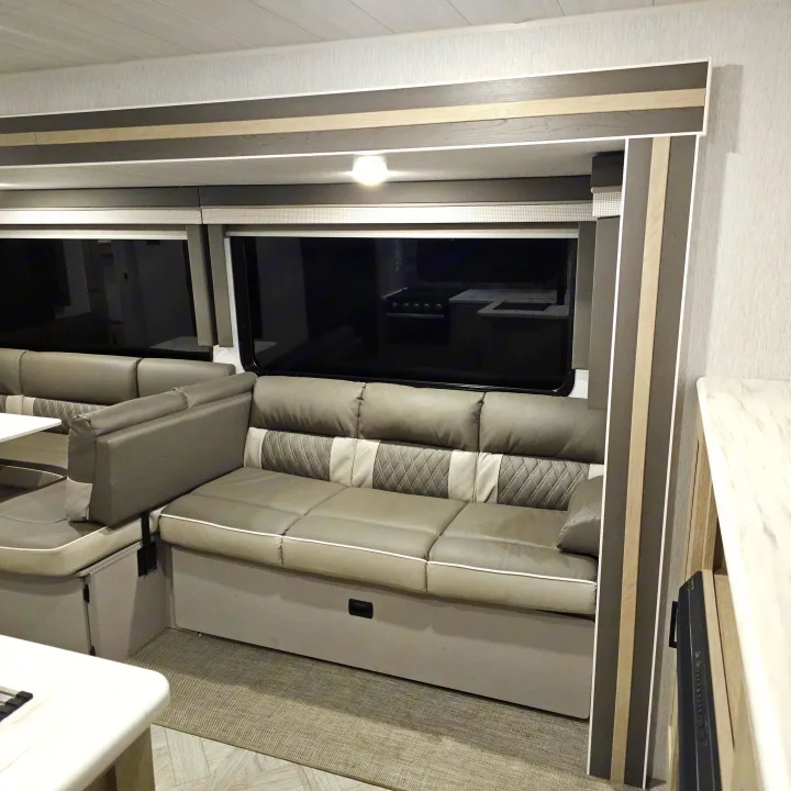 RV rental interior with a modern grey dinette seating, light wood paneling, and large windows revealing a kitchen reflection.. Forest River Salem Platinum 2023