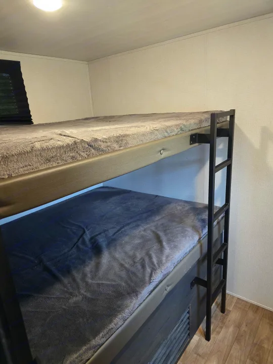 Cozy RV rental bunk beds, featuring soft grey blankets & a black ladder, a practical sleeping space.. Keystone RV Hideout 2023