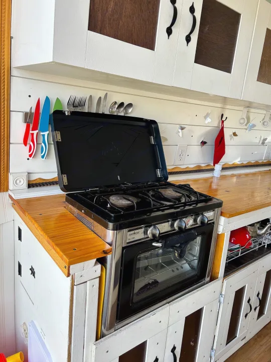 A compact RV rental kitchen featuring a Camp Chef oven/stove, wooden countertops, and wall-mounted utensils.. Ram Dodge Promaster 3500 2019