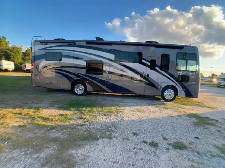 Modern gray RV motorhome, available for rv rental, parked outdoors on gravel with blue sky.. Thor 33.2 2020