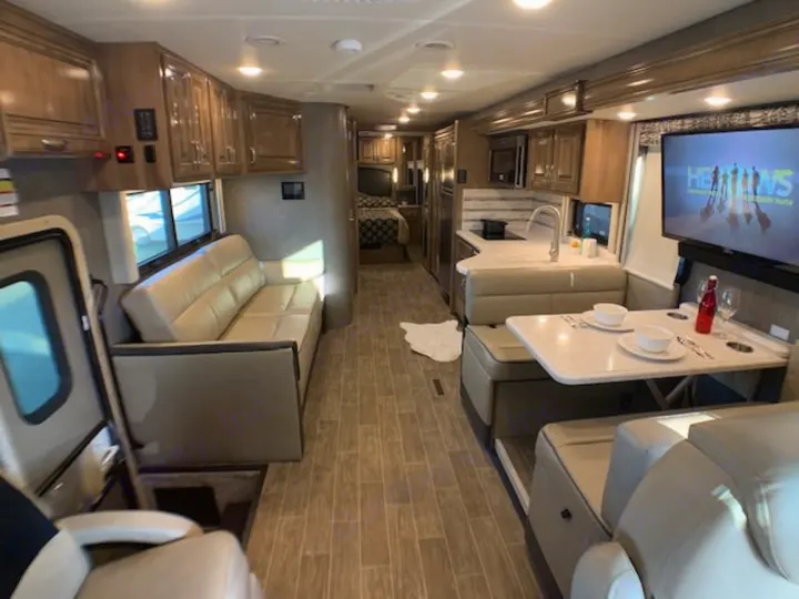 Spacious RV interior showing a modern kitchen, dining booth, sofa, and TV. The rear bedroom is visible. Great rv rental!. Thor 33.2 2020
