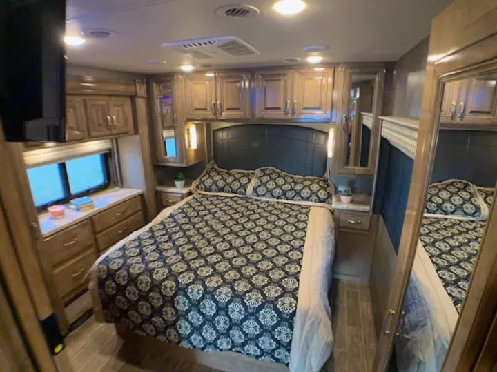 Comfortable RV rental bedroom featuring a large bed, ample storage cabinets, and a window. Perfect for your next trip.. Thor 33.2 2020