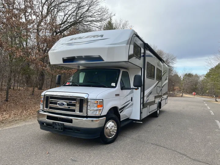 White Solera motorhome for RV rental, parked on an asphalt road near bare trees under a cloudy sky.. Forest River Solera 27 DSE 2023