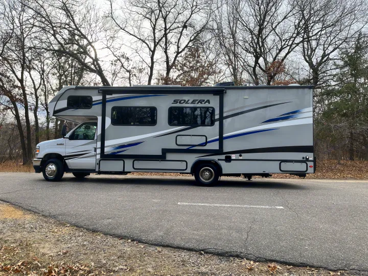This grey Class C RV rental is parked on an asphalt road with bare trees, ready for adventure.. Forest River Solera 27 DSE 2023