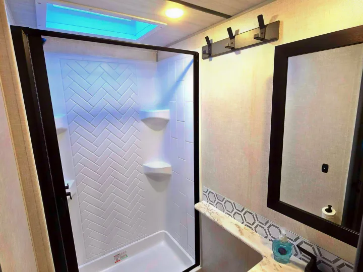Inside this RV rental: a modern, well-lit bathroom featuring a shower with herringbone walls, skylight, and vanity.. Forest River Surveyor Legend 2023