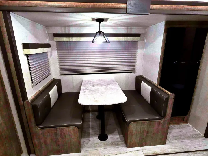 Cozy RV rental dinette featuring comfortable booth seating, a central table, window blinds, and overhead lighting.. Forest River Surveyor Legend 2023