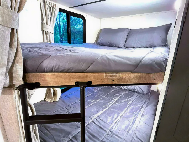 Cozy RV rental interior featuring comfortable bunk beds with grey bedding, perfect for restful nights on your travels.. Forest River Surveyor Legend 2023