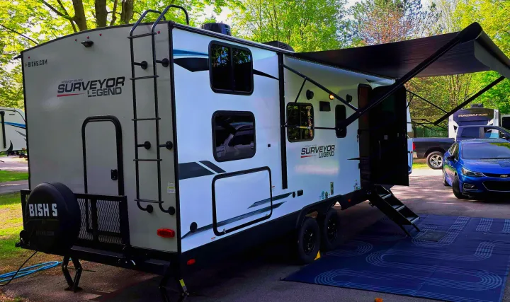 Forest River Surveyor Legend RV rental fully set up at a campsite with extended awning, ladder, and outdoor mat.. Forest River Surveyor Legend 2023