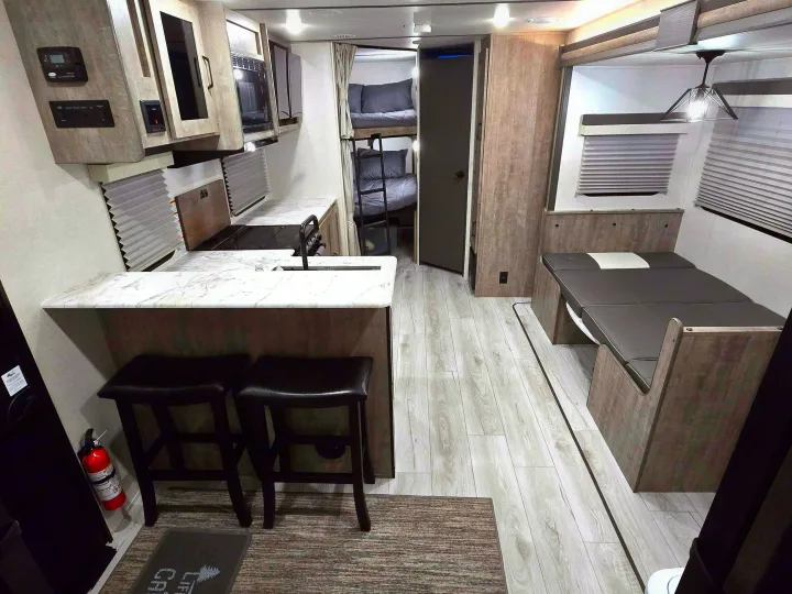 This RV rental interior features a kitchen, dinette, and bunk beds, offering a modern and functional living space.. Forest River Surveyor Legend 2023