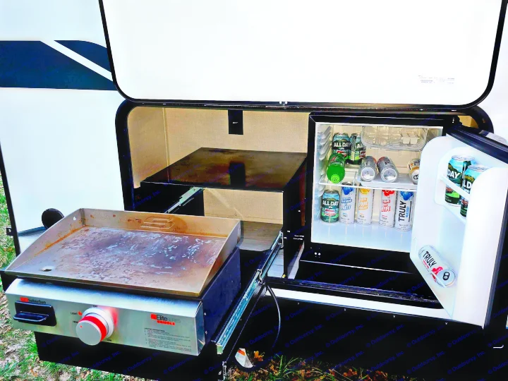 This RV rental outdoor kitchen features a pull-out griddle and a stocked mini-fridge, ready for delicious meals and cold drinks.. Forest River Surveyor Legend 2023